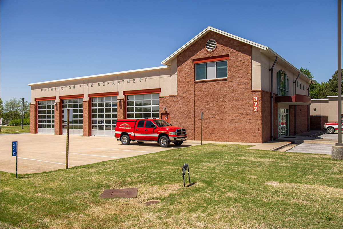 Exterior view of a modern Farmington Fire Station with large bay doors, a red fire truck parked outside