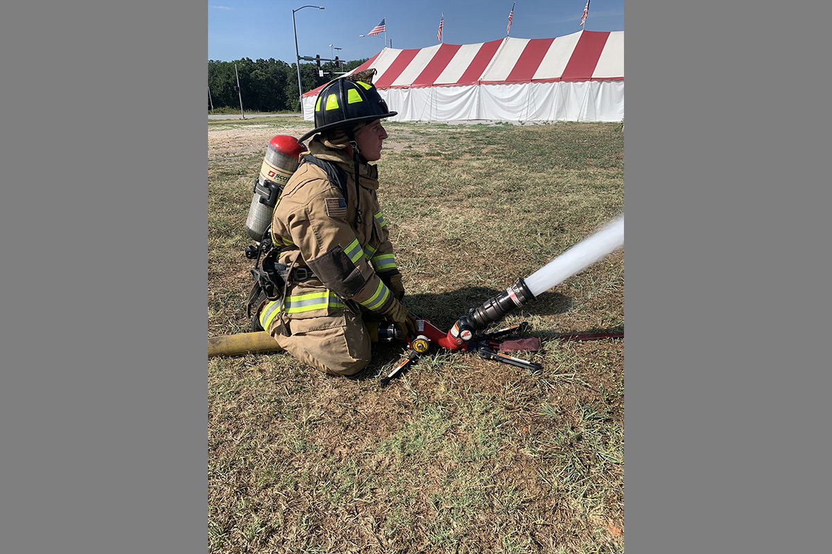 Firefighter in full gear operating a hose with a nozzle attached, spraying water