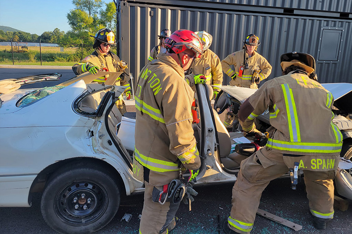 Firefighters using hydraulic rescue tools to extricate a person from a damaged white car after an accident