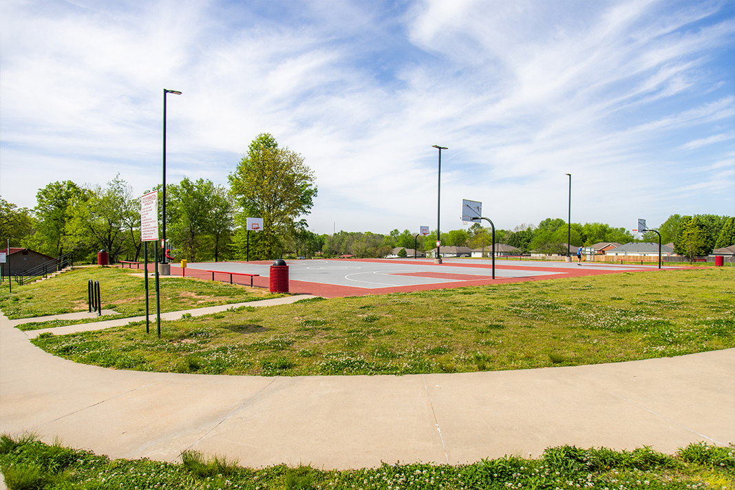 Basketball courts in Farmington park with bright red and gray surfaces, walking paths, and green fields surrounded by trees