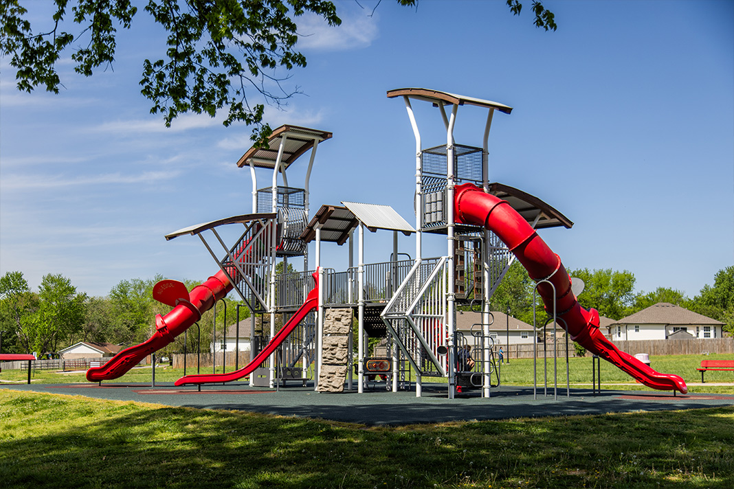 View of a modern playground in Farmington park featuring a large red spiral slides 